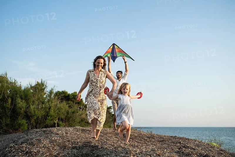A joyful family of three enjoys a sunny day on an Italian beach, flying a colorful kite and creating cherished memories by the sea. Perfect example of family fun