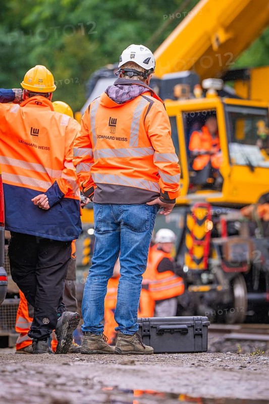 Construction workers in orange protective clothing and white helmets in front of a construction crane in rainy weather, track construction, Hermann Hessebahn, Calw, Black Forest, Germany