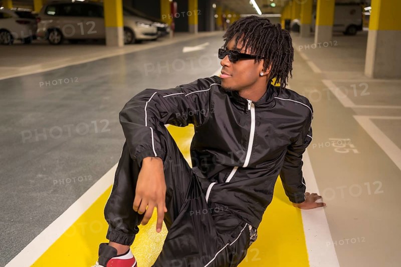 Portrait of an african music artist looking away sitting on an urban garage