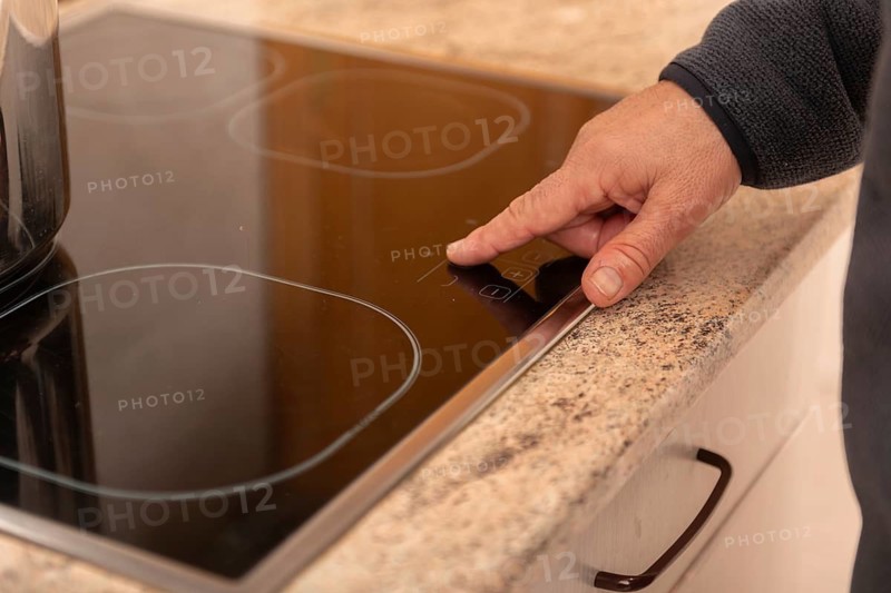 A close up view of a hand using the touchscreen control on a modern induction stove top. The sleek, minimalist design blends seamlessly with the granite counter top