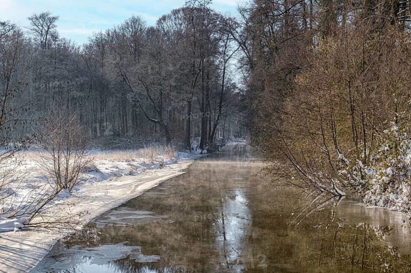 A quiet river in a snowy winter forest with trees and sky reflection, River Dinkel, Legden, Münsterland, North Rhine-Westphalia, Germany