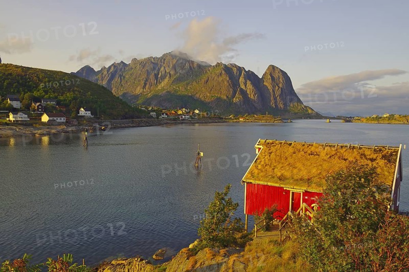 Red wooden hut with boat on the fjord shore, surrounded by mountains at sunset, Rorbuer, holiday accommodation, Reine, Moskenes, Lofoten, Nordland, Norway