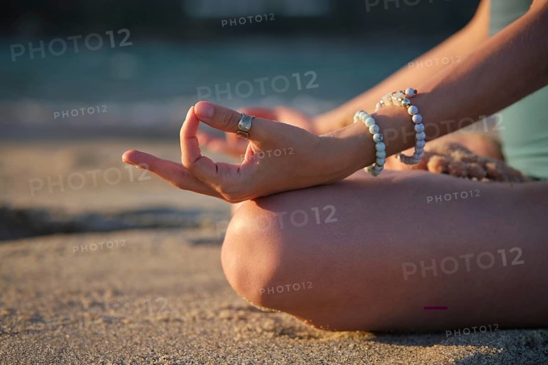 Close-up of a woman in Padmasana lotus pose, meditating on the beach with a peaceful hand gesture at sunset