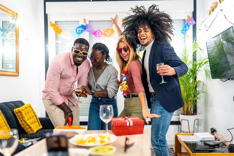 Happy young friends of different ethnicity dancing during home birthday party