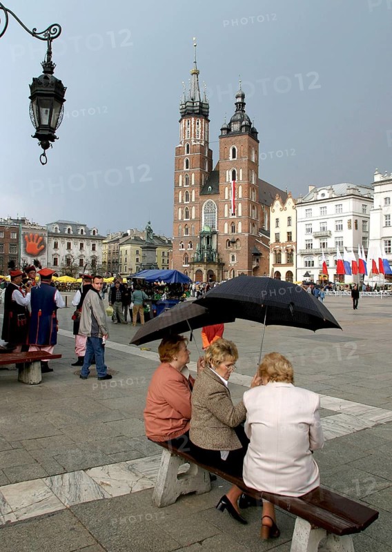 Krakow, POL, 01.05.2004 - Tourists protect themselves with umbrellas on the market square in Krakow (Rynek), with St Mary's Church in the background, Poland