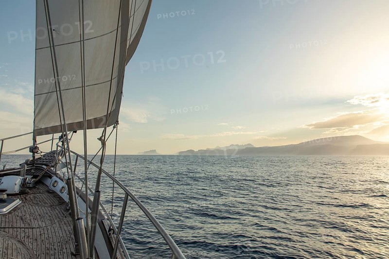 A sailboat gracefully cruises on the calm waters of the Mediterranean Sea, with the golden glow of the sunset in the background near the scenic Costa Blanca coastline