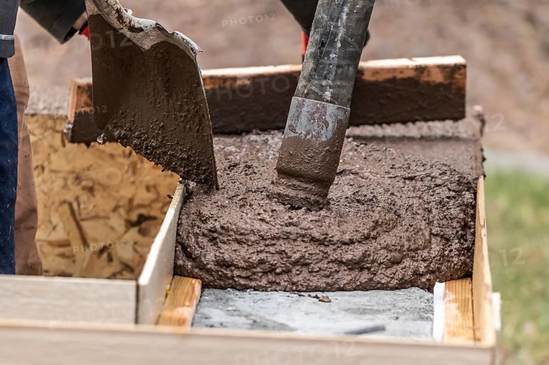 Construction Worker Leveling Wet Cement Into Wood Framing