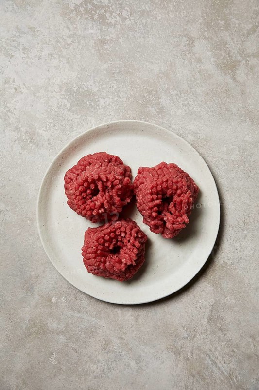 Three mounds of freshly ground beef presented on a white ceramic plate. The meat's rich red color and texture provide a vivid display, perfect for culinary themes