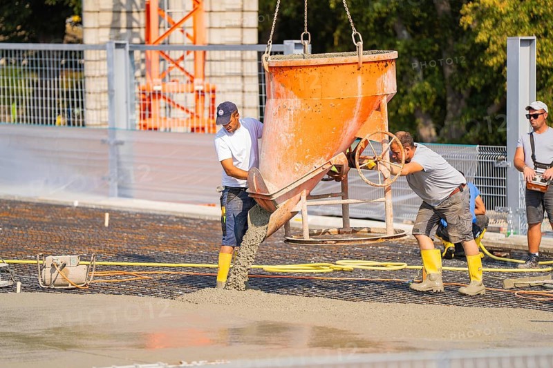 Two construction workers empty concrete from a large container on a construction site, Parkhausbau, Calw, Germany