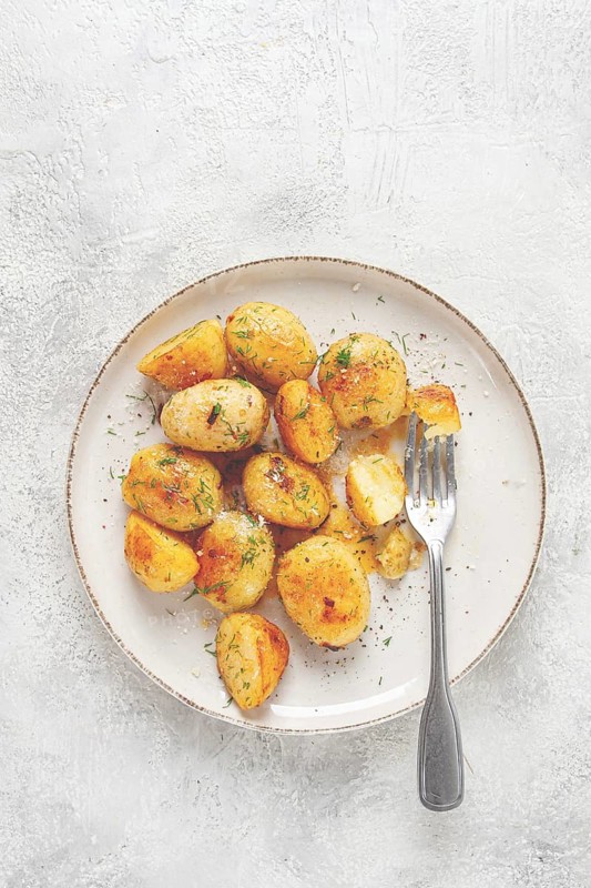 Half-eaten fried new potatoes, with butter and dill, on a white plate, with a fork, at home, no people