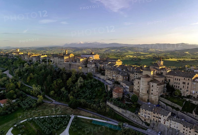 Captivating aerial view of Treia, Italy, bathed in golden sunset light. The historic architecture is surrounded by lush landscapes, offering a serene and picturesque scene