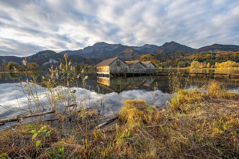 Boathouses in the lake at sunrise, Lake Kochel in autumn with reflection, behind mountain peaks Herzogstand and Heimgarten Upper Bavaria, Bavaria, Germany