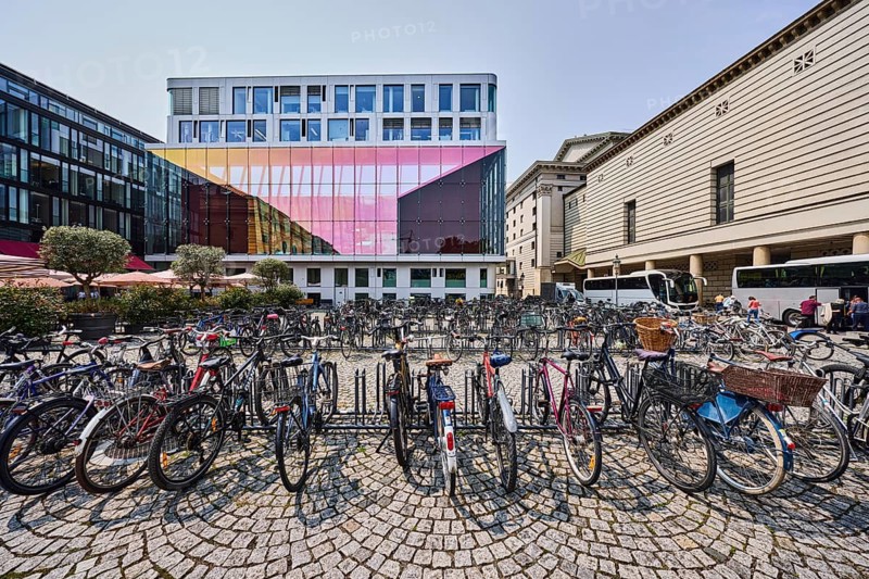 Rehearsal stage Bayerische Staatsoper, modern architecture, general buildings, roads, square, barrier bollard, bicycle rack with bicycles, street made of paving stones, trees, pale blue sky, cumulus clouds, cirrostratus clouds, slightly diffused and sunny light, Marstallplatz, Alfons-Goppel-Straße, Munich, state capital, district-free city, Bavaria, Germany