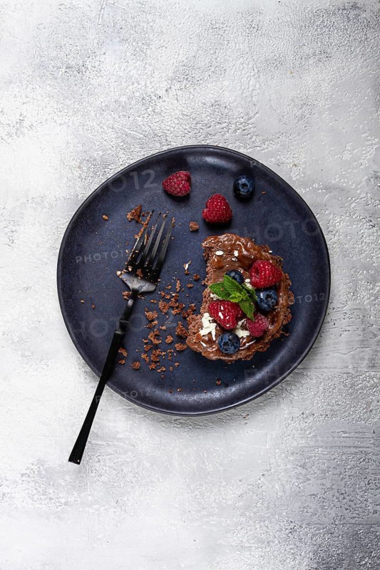 Half-eaten chocolate tartlet, on a plate, stuffed with cottage cheese and berries, breakfast, homemade, no people