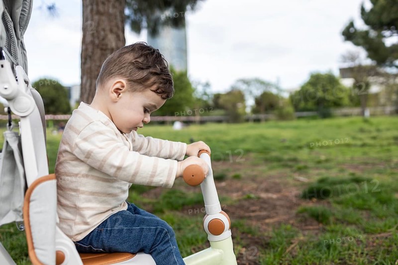 A curious baby enjoys a sunny day in the park, riding a tricycle and exploring the green surroundings. The child is dressed in casual attire, embracing the outdoor adventure