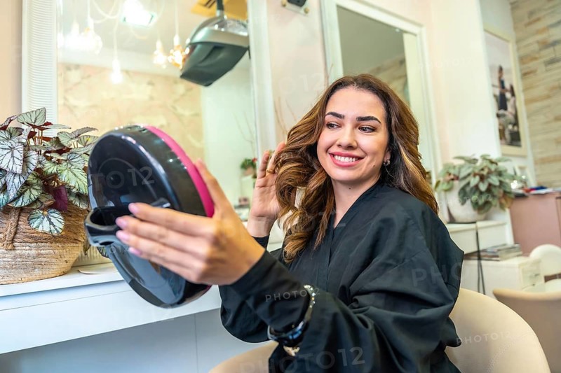 Smiling woman checking her fresh haircut and styling in a handheld mirror at a professional hair salon, feeling confident and satisfied with the beauty treatment