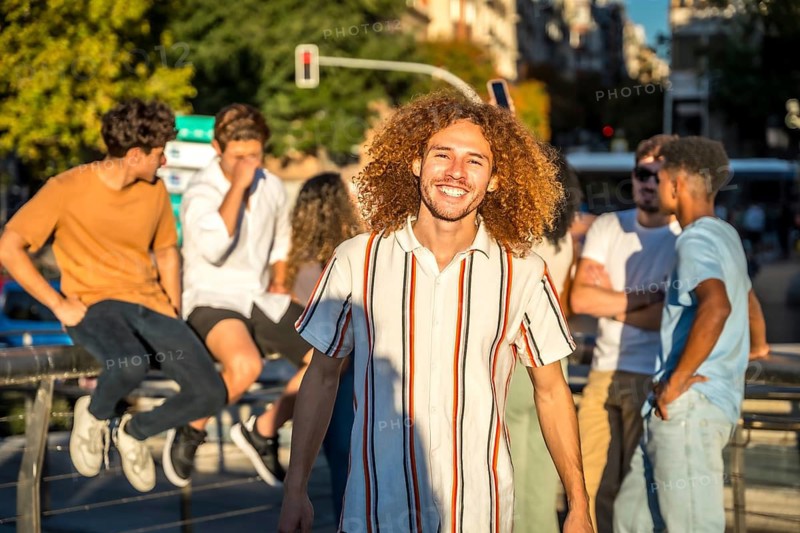 Portrait of smiling young man with curly hair and friends in the city during sunset