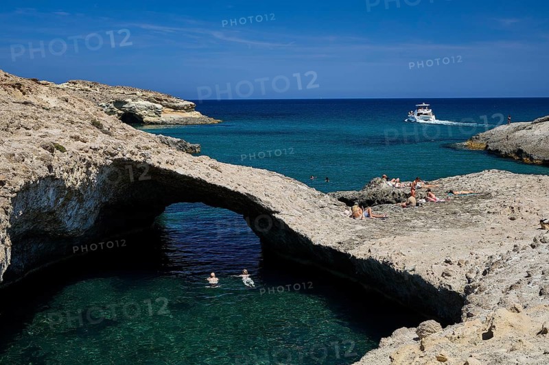 A boat passes by while people sunbathe and swim on the rocky shore, Kapras, Kapros, Beach, Kapros Beach, Caves, Paralia Kapros, Milos, Cyclades, Greek Islands, Greece