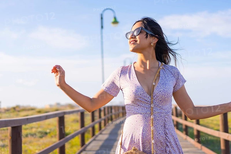 Portrait of caucasian brunette woman smiling on summer vacations next to the beach sand on a walkway