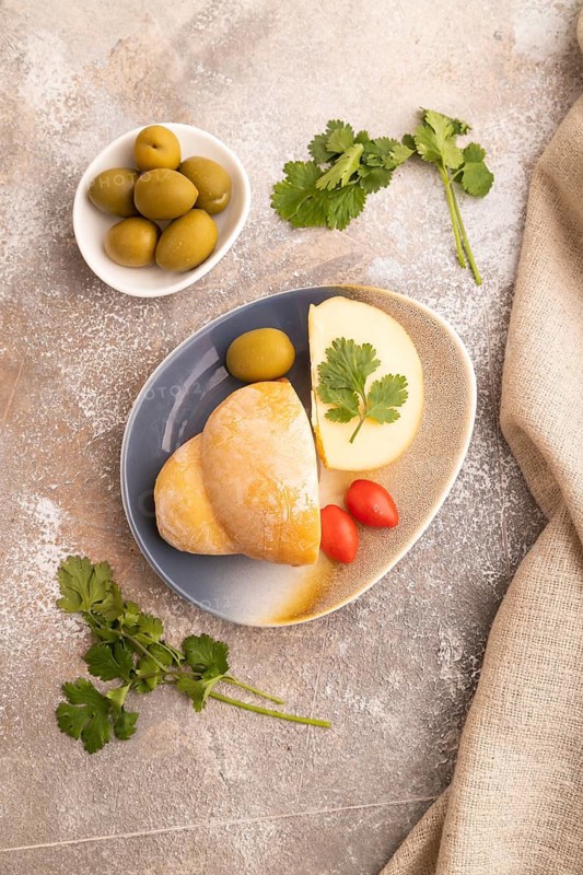 Smoked Mozzarella cheese, with tomatoes and olives on brown concrete background and linen textile, top view, flat lay, close up