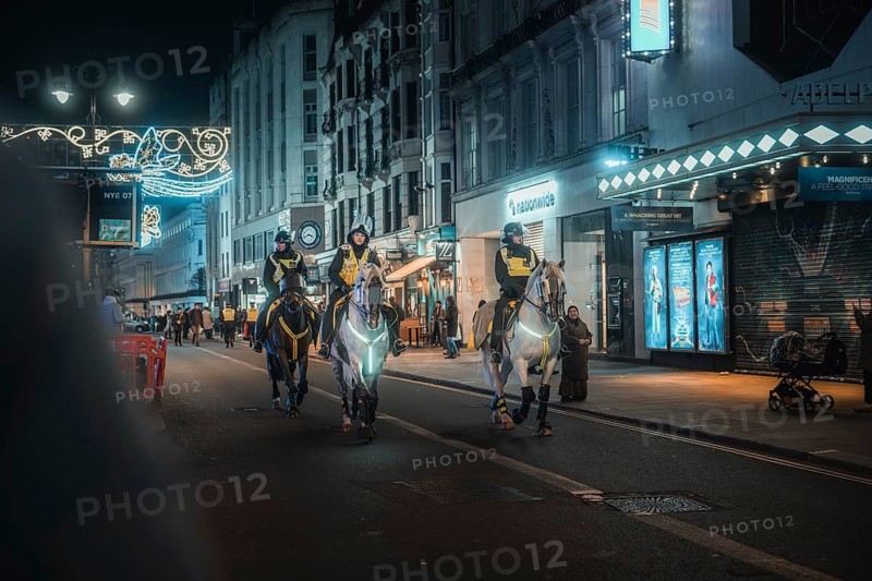 Police on horses patrol illuminated urban street at night, New Year's Eve London, United Kingdom
