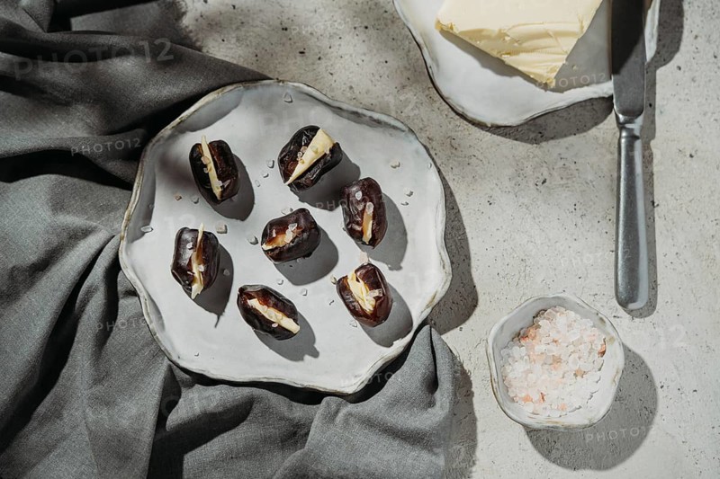 Butter stuffed dates are elegantly presented on a rustic ceramic plate. With sea salt sprinkled on top, they make a chic, sophisticated appetizer on a textured background