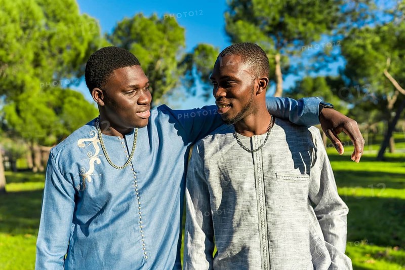 Two young senegalese men wearing traditional dashiki clothing walk together in a park, embracing friendship during the holy month of ramadan