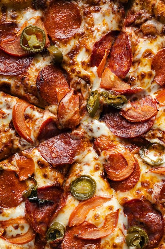 Close-up view of a mouth-watering pepperoni pizza loaded with cheese, sliced peppers, and onions, perfect for any meal