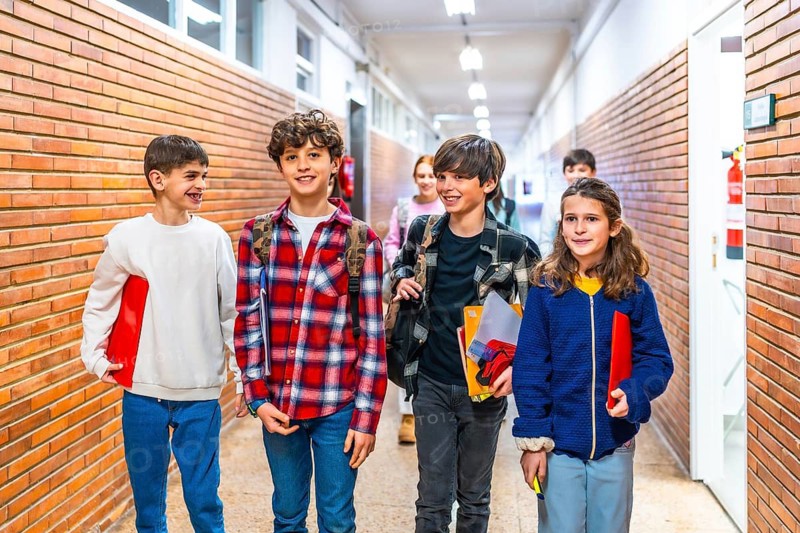 Smiling pupils carrying books and backpacks are walking in school corridor between classes