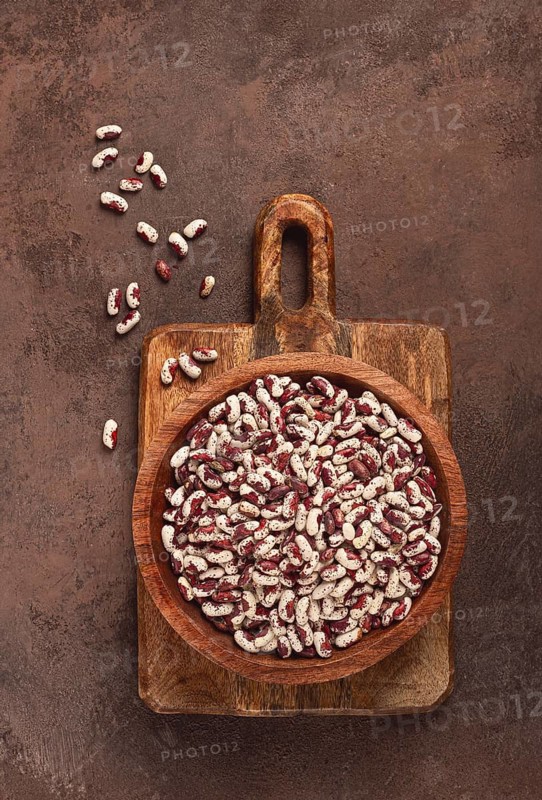 Variegated beans, red with white spots, raw in a wooden bowl, top view, no people
