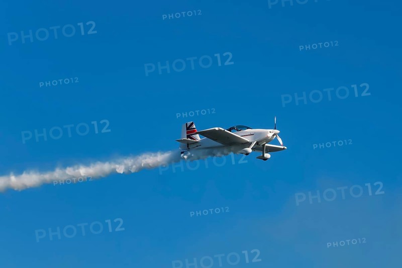 Stunt aerobatic plane performing stunts in blue sky with smoke trail. Concept of speed, difficulty, precision, risk, challenge