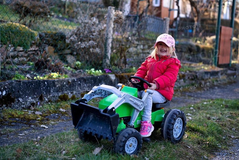 Little girl, 3 years, blonde, baseball cap, logo NYY New York Yankees, rides on toy tractor, tractor, tractor, vehicle, toy, Stuttgart, Baden-Württemberg, Germany