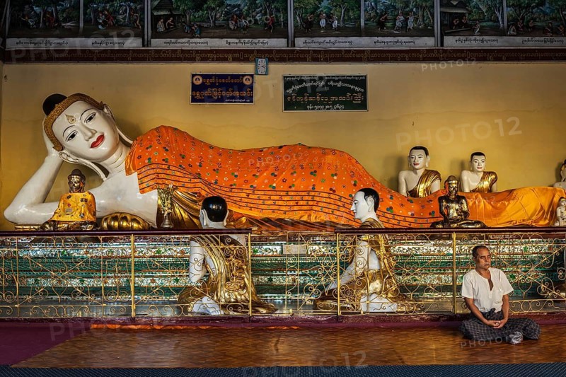 YANGON, MYANMAR, JANUARY 3, 2014: Man meditating near statue of Recumbent Buddha in Shwedagon Paya pagoda