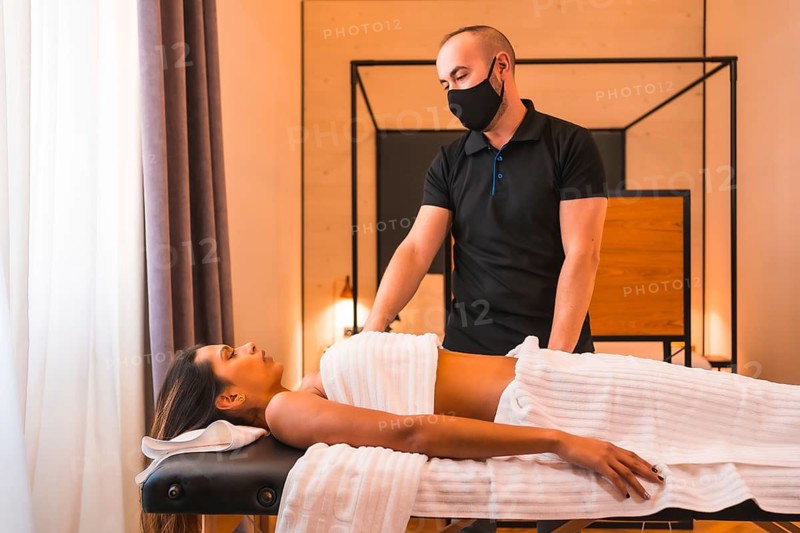 Massage at home, a young man performing a massage at the client's home, a little before explaining the process. With a face mask in the coronavirus pandemic
