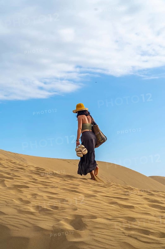 Young woman tourist walking barefoot carrying sandals on the maspalomas dunes in gran canaria, spain, enjoying summer vacation