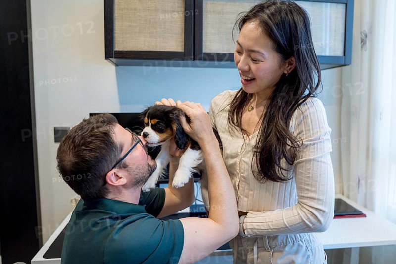 A diverse couple enjoys a tender moment with their puppy in a cozy home setting. The cheerful atmosphere captures the warmth and joy of their shared life together