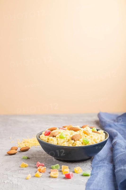 Millet porridge with candied fruits and almonds in blue ceramic bowl on a gray and orange background and blue linen textile. Side view, close up, selective focus, copy space