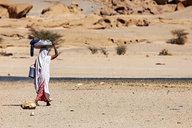 A single person carries loads in the remoteness of the desert, woman washing clothes in the Sahara in Algeria