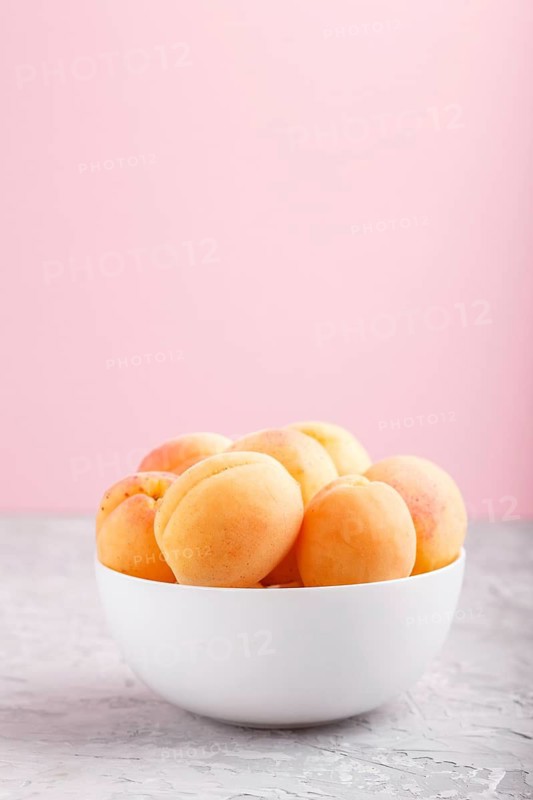 Fresh orange apricots in white bowl on gray and pink pastel background. side view, copy space, selective focus