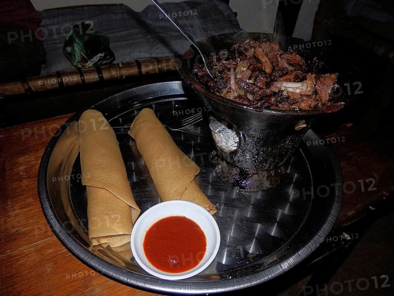 A tray of injera and wot, a meat dish and a bowl of chili sauce, Ethiopia