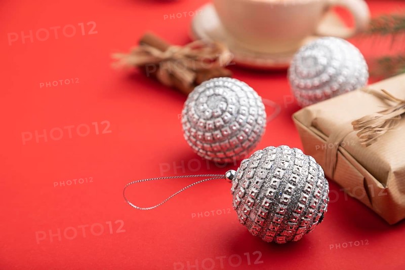 Christmas or New Year composition. Decorations, box, cinnamon, silver balls, fir and spruce branches, cup of coffee, on a red paper background. Side view, close up, selective focus