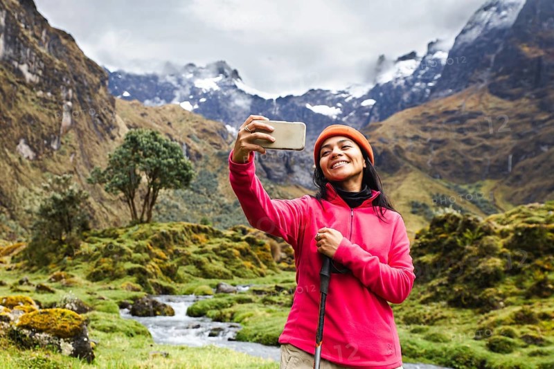 Ecuadorian woman wearing a pink jacket takes a selfie with a stunning backdrop of El Altar volcano, Ecuador. Snowy peaks and lush greenery create a breathtaking scene