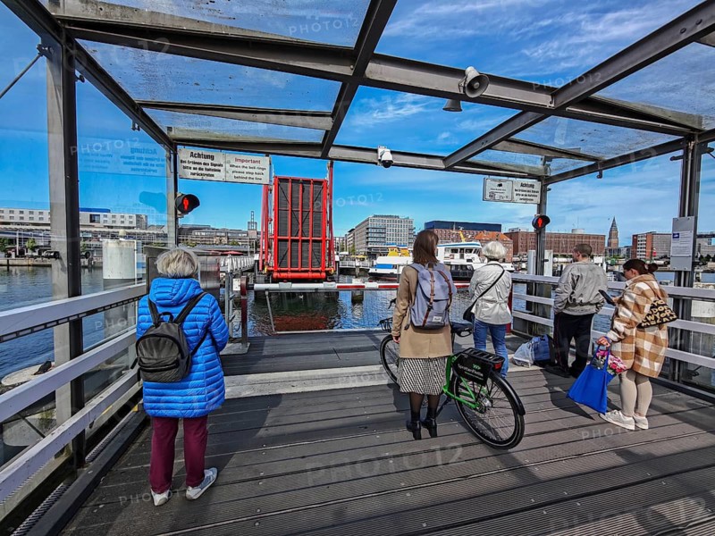 Hörnbrücke connects the west bank with the east bank district Gaarden, the pedestrian and bicycle bridge is a rare three-span folding bridge, waiting pedestrians and cyclists, pedestrian traffic light on red, barrier closed, warning signs, temporarily no passage, passage of ships, technology, wood and metal construction, maritime atmosphere, blue sky and sunshine, Baltic Sea, Kiel, Schleswig-Holstein, Germany