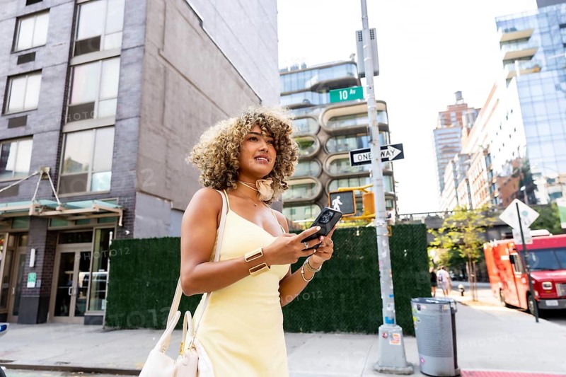 Woman with curly hair exploring a new york city street, holding a mobile phone and navigating the urban environment, embodying the lifestyle of a modern city dweller