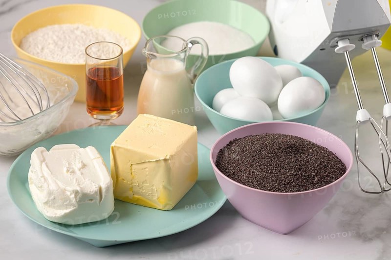 Baking ingredients such as poppy seeds, eggs, butter, milk and rum on a work surface