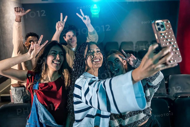 Cheerful young people taking a selfie with smartphone while watching a movie at the cinema, enjoying a fun night out with friends