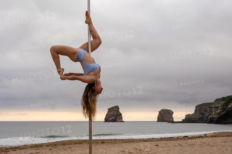 Young caucasian girl doing pole dance at sunrise at a beautiful beach. pole dance acrobatics on the sand of Hendaya beach, France
