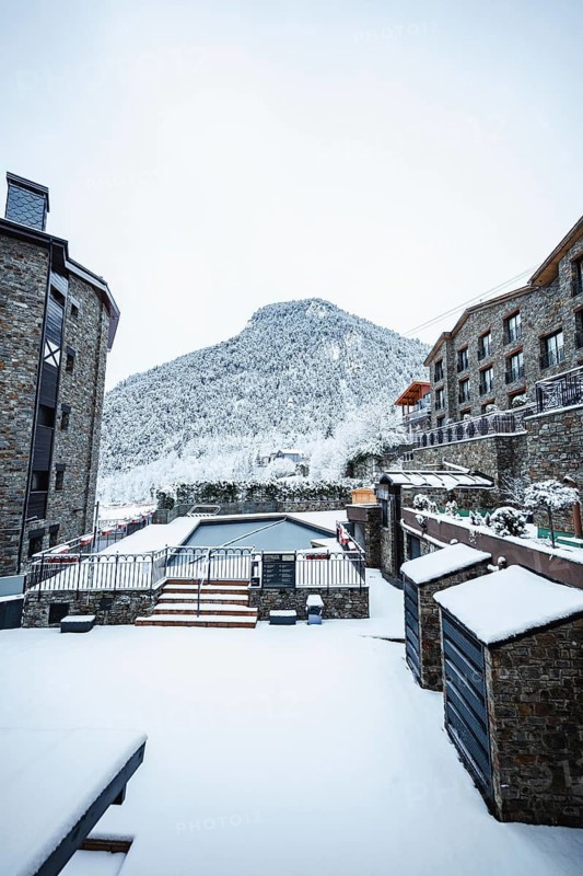 A picturesque village nestled in the mountains, with stone buildings and a snow blanketed landscape, creating a serene and tranquil winter wonderland scene in Andorra