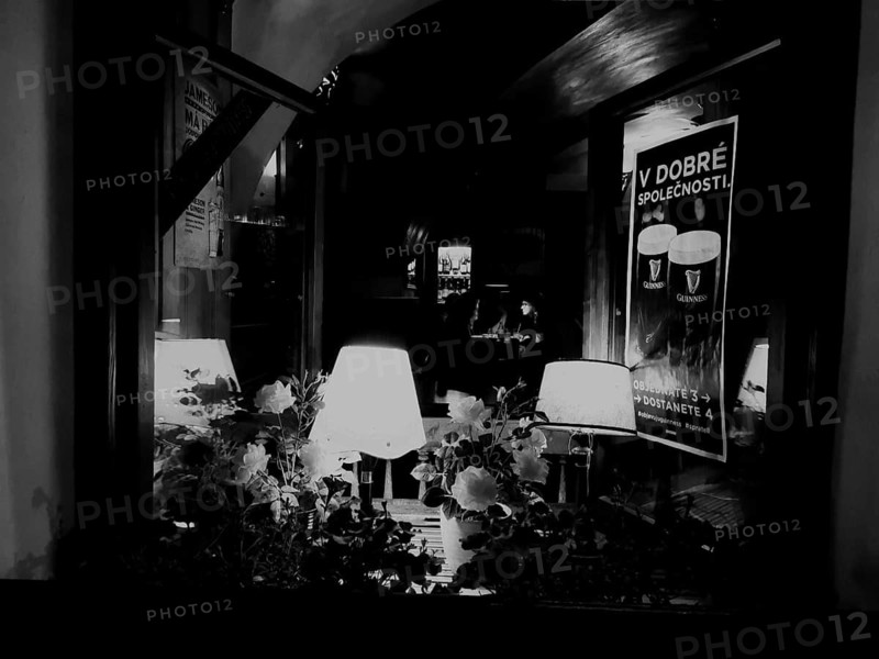 Cosy café with warm lighting from lamps, atmospherically accentuating the inviting ambiance inside, monochrome, Prague