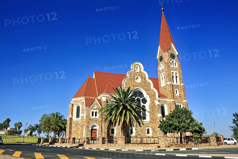 A historic church with a red roof against a clear blue sky, surrounded by trees, The historic German Church in Windhoek Namibia